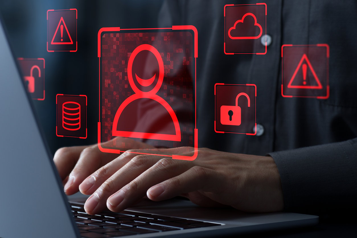 Ghost Credentials displayed in images of red warnings and creep people icons of an IdM staff's laptop screen representing the Physical Security Risk in Employee Offboarding