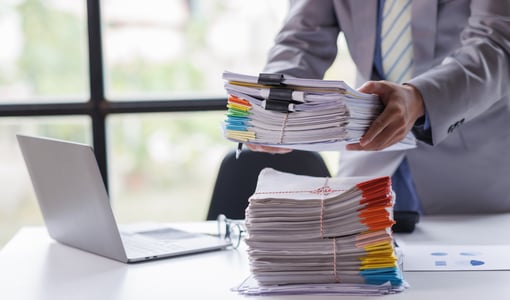 Stack of Paper next to a laptop because transferring paper records to the Cloud is easy